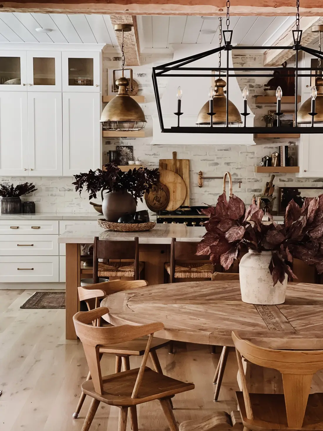 White kitchen with a whitewashed brick backsplash, warm wood furniture, brass pendant lights, and a black chandelier