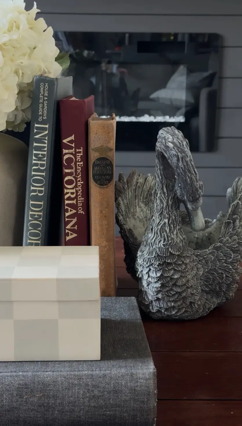 Vintage books including Victorianna standing beside a stone swan and a cream checkerboard box