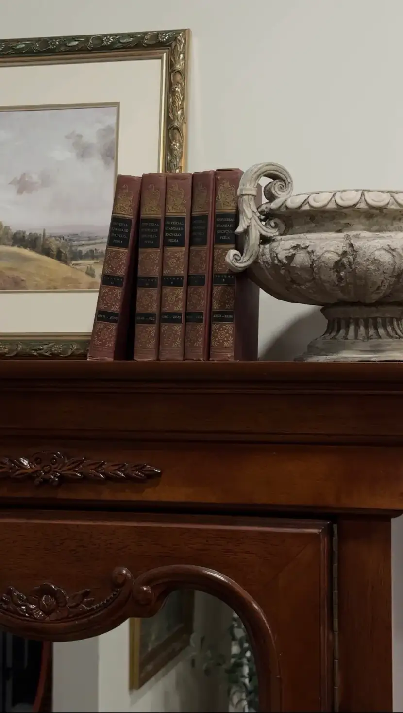A matching set of leather-bound books and a stone urn on a carved wood dresser