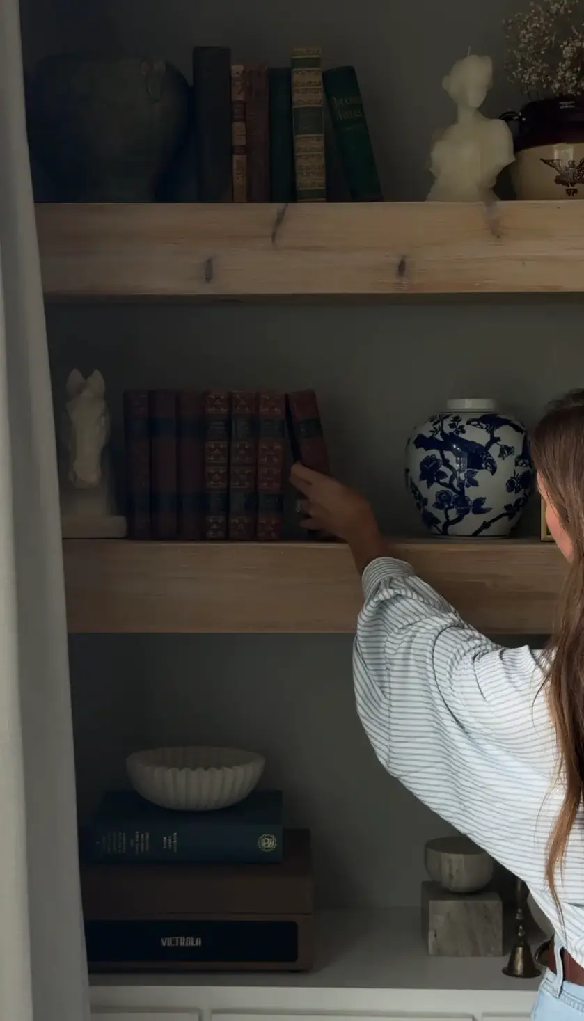 Logan reaching for a vintage book on an oak shelf styled with pottery and a small horse figure