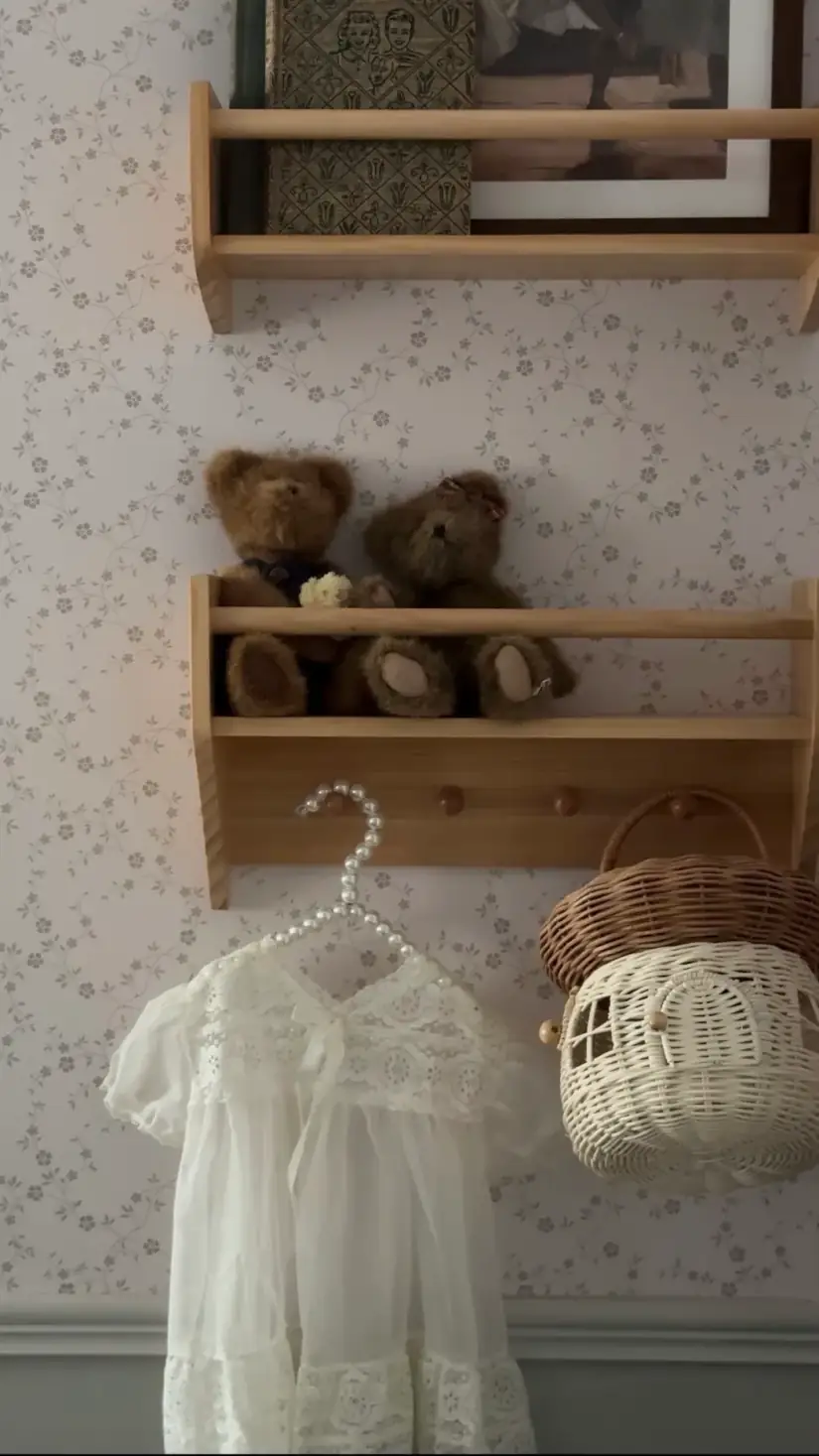 Two teddy bears on a peg rail above a white child’s dress and a wicker basket