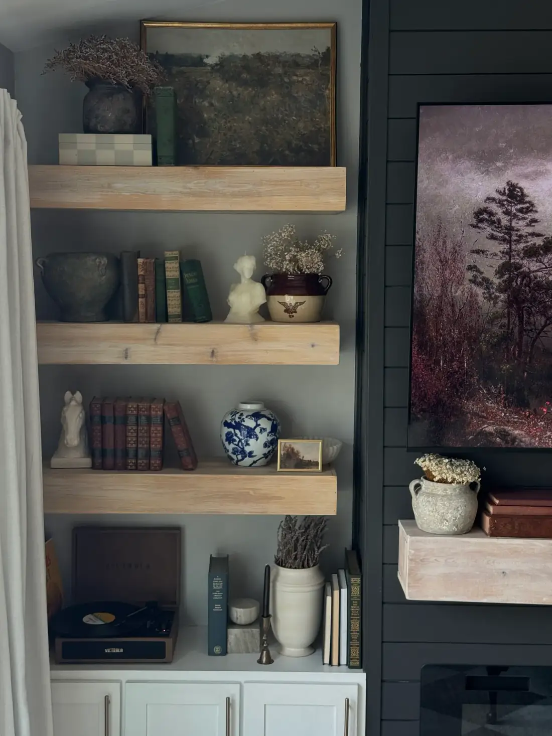 Open oak shelves styled with vintage books, pottery, a record player, and a landscape on the neighboring black wall